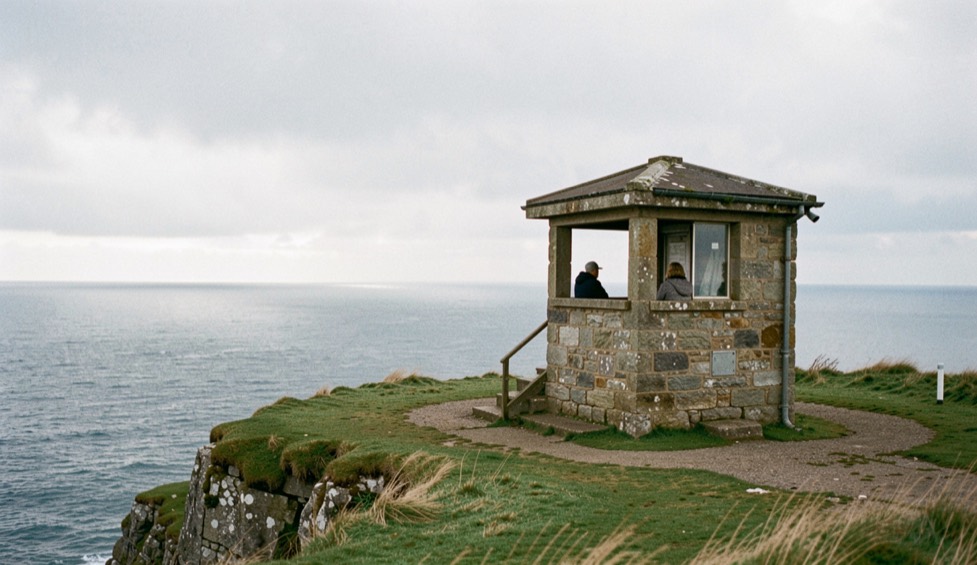 A stone lookout shelter on a cliff top with the open sea behind it and low cloud