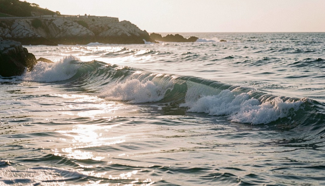 Long low swell running past a rocky point with the sun low and the water in silver light