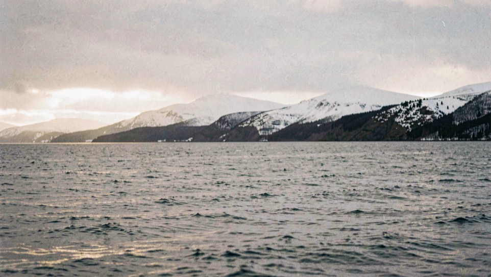 Low winter sun across a cold grey sea with snow on the hills behind a dark shoreline